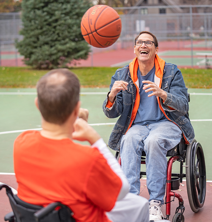 Two men in wheelchairs playing basketball outside