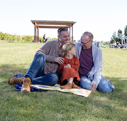 Two guys and a little girl on a blanket outdoors